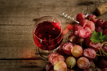 Glass of red wine and Fresh ripe pink grape on a vintage plate, on an old wooden background....