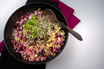 Bowl of quinoa beet salad with seeds and chopped green onions. Dark backround.