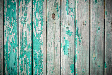 Fototapeta na wymiar Background in grunge style. Wooden old fence with peeling paint. From vertical boards of turquoise color. With dark vignette around the edges.