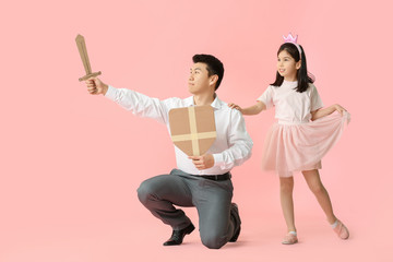 Asian man and his little daughter dressed as prince and princess on color background