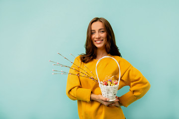 Studio shot of a young european woman with shirt hairstyle wearing bright clothes posing with holiday Easter basket posing over blue background