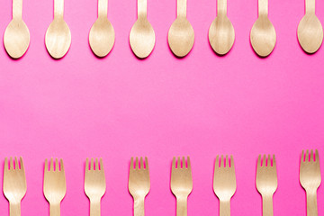 eco-friendly disposable wooden forks and spoons laid out on top and bottom of the sheet on a pink...