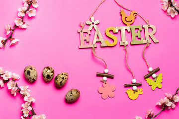 four quail eggs and the wooden inscription "Easter" near the flowering branches arranged in a circle on a pink background. place for text.
