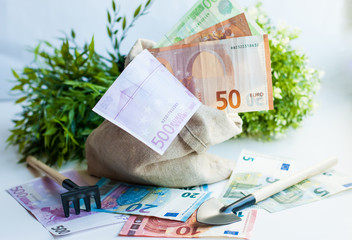 Gardening tools and money. A bag of money, making a ton of money. Dollars and euros