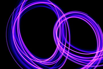 Long exposure photograph of neon purple streaks of light in an abstract swirl, parallel lines pattern against a black background. Light painting photography.