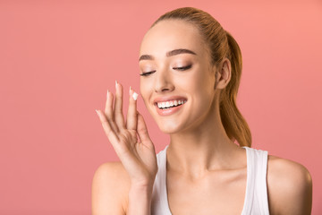 Obraz na płótnie Canvas Happy Woman Applying Facial Cream For Skin Nourishment, Pink Background