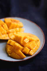 Cut mango halves on a plate. Selective focus, dark blue background.