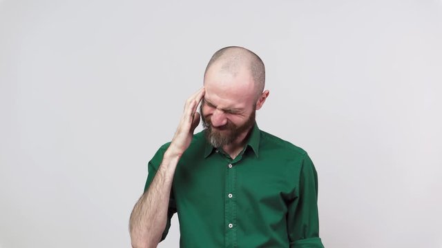 Portrait of bearded man having headache isolated over white background. Sick unhappy man rubbing temples. Concept of emotions.