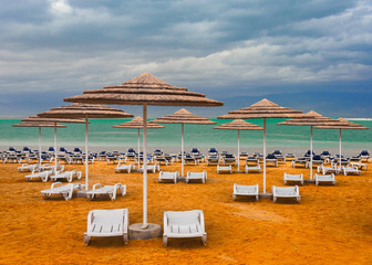 Empty beach with sunshade and chaise lounges against the cloudy sky.