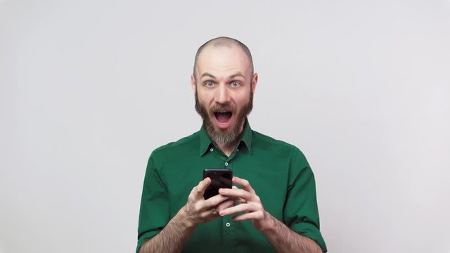 Handsome happy bearded man using mobile phone over white background. People sincere emotions, lifestyle concept. Looking surprised using cell phone.
