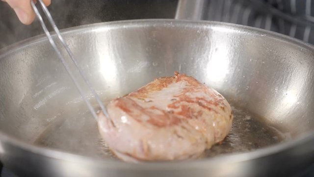 Hand of unrecognizable male chef flipping piece of duck meat frying in hot pan with olive oil. Slow motion footage. Cooking classic Confit Duck in French restaurant, close-up. Shot in hd.