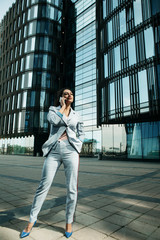 woman dressed in business style against the background of a business center is holding a mobile phone