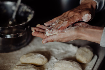 cook with bare hands in flour sculpts dough pies on the kitchen table © Ilya.K