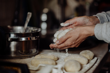 cook with bare hands in flour sculpts dough pies on the kitchen table © Ilya.K