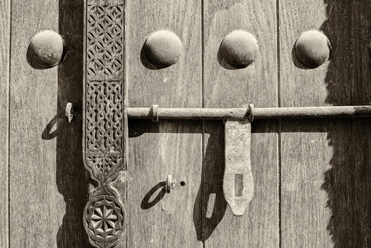 Sepia detail of a carving, doornails and lock on a traditional wooden Arabian door.