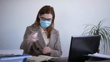 coronavirus pandemic, a young businesswoman in a medical face mask uses an antiseptic to prevent viruses and infections, disinfection of a smartphone and laptop keyboard, quarantine - Powered by Adobe