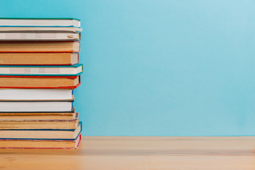 A simple composition of many hardback books, raw books on a wooden table and a bright blue background. Going back to school. Copy space. Education.