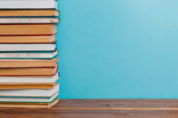 A simple composition of many hardback books, raw books on a wooden table and a bright blue background. Going back to school. Copy space. Education.