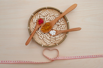 Voedingssupplementen in houten lepels in een gevlochten bamboe bord met een hartvormig meetlint. Detailopname. Concept: gezonde levensstijl.