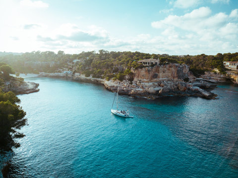 Drone panoramic image moored yachts on bright blue bay Cala Blanca Andratx, Palma de Mallorca, rocky coast breathtaking view, Balearic Islands Spain.