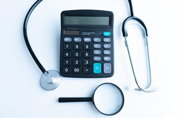Concept of medical expenses or medical insurance for blog title and header. Stethoscope,white calculator and magnifying glass on wooden background.
