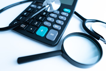 Concept of medical expenses or medical insurance for blog title and header. Stethoscope,white calculator and magnifying glass on wooden background.