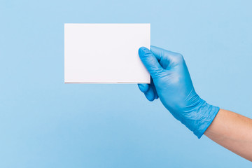 Fototapeta premium female hand in a medical glove holds a blank form of paper on a blue background. Mock up, business card
