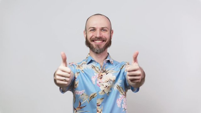 Happy bearded man wearing hawaiian shirt showing thumbs up over white background. Good job, very well.