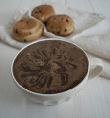 a large cup of coffee with buns in the background