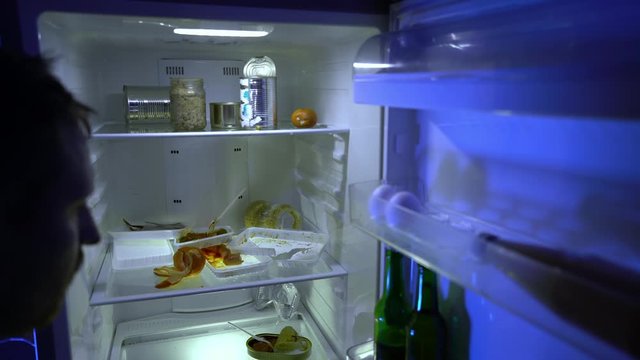A man during self-isolation is looking for food in the refrigerator. Leftover food in the refrigerator during quarantine. The ban on leaving the house on the street. Stay at home. Coronavirus.COVID-19