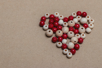 Many beautiful red and brown beads made of plastic and wood in the shape of a heart lie on a sheet of cardboard. Heart as a symbol of love, holiday Valentine's Day.