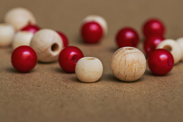Many beautiful red and brown beads made of plastic and wood are scattered on a sheet of cardboard. Photographs under natural light. Materials for home needlework and comfort.