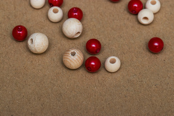 Many beautiful red and brown beads made of plastic and wood are scattered on a sheet of cardboard. Photographs under natural light. Materials for home needlework and comfort.
