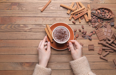 Fototapeta premium Female hands with cup of hot chocolate and cinnamon on wooden background