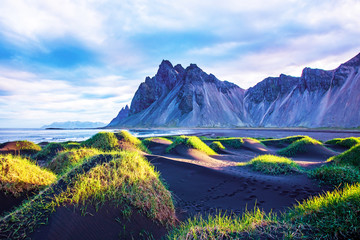Scenic landscape with most beautiful mountains Vestrahorn on the Stokksnes peninsula and cozy lagoon with green grass on the sand dunes at sunset in Iceland. Exotic countries. Amazing places.