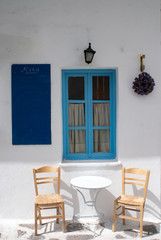 A small cafe on the beautiful Greek island of Paros.  A table and chairs by a shuttered window in the village of Naoussa.