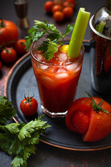Classic alcoholic cocktail Bloody Mary with ice, lemon and celery. Cocktail ingredients and bar tools on a dark vintage table. Vertical 