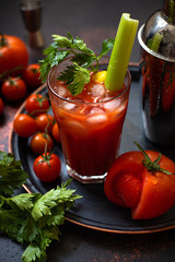 Classic alcoholic cocktail Bloody Mary with ice, lemon and celery. Cocktail ingredients and bar tools on a dark vintage table. Vertical 