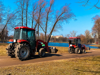 Red tractors trucks in spring city park. Cleaning. Early spring. Works. Sunny spring day.