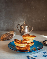 Homemade pancakes on a blue ceramic plate, metal sugar bowl and paper napkins on a white table