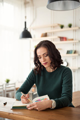 portrait of a young thinking woman in lifestyle sitting at the table and writing notes in a...
