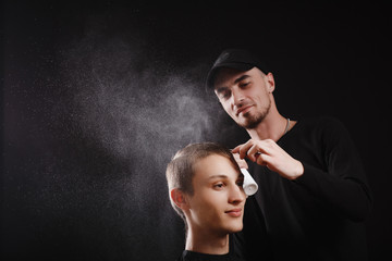 Hairdresser or barber sprinkles water on the client's hair, holding a comb in modern barbershop on black background.