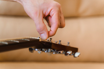 Detail of guitar neck and strings of the guitar tuned by turning the pegs. Unrecognizable man...