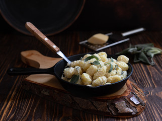 Italian homemade gnocchi with butter and sage served in a pan on a wooden cutting board. Italian food. Wooden table. Dark background. Copy space