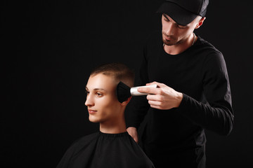 Making haircut look perfect with a brush. Young man getting haircut by hairdresser while sitting in chair at barbershop on black background.