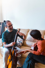 Side view of woman receiving musical course in her house. Leisure and artistic hobby indoors. Indoor music class at home. Teacher explaining guitar lessons to young female student.