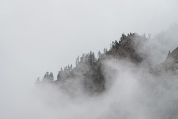 Ghostly alpine view through low clouds to beautiful rockies. Dense fog among giant rocky mountains...