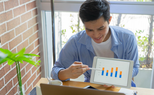close up young asian employee man video conference with marketing team and showing market research  by tablet and explaining report in ouse for quarantine and work from home concept