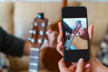 Unrecognizable woman recording music online class with smartphone. Guitar lessons at home. Screen shot of musical course. Technology and leisure indoors. Professor teaching to play an instrument.