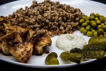 Delicious buckwheat porridge with chicken, green peas, cucumbers and sauce on a white plate. Tasty chicken skewers from fillet on a white plate. Healthy and tasty  food with chicken meat.